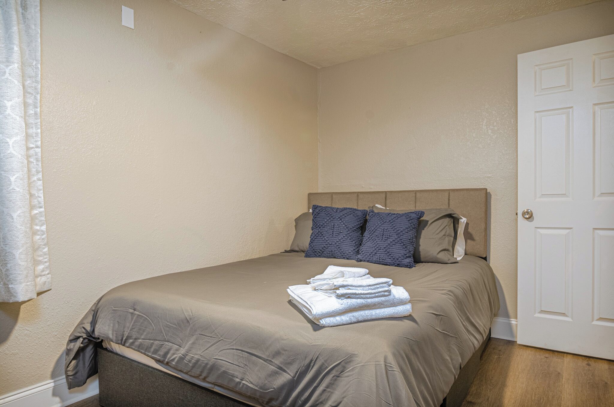 Un lit simple avec une tête de lit et des oreillers de couleur beige, une serviette pliée sur le lit et une porte blanche sur la droite.