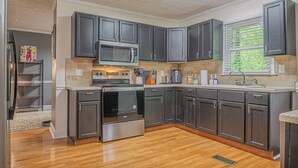 A modern kitchen with dark cabinets, stainless steel appliances, and a window with blinds. - Cozy Bungalow Retreat w FirePit & Grill (Columbus)