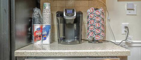 A kitchen with dark cabinets, a stainless steel dishwasher, a coffee maker, and a coffee pod holder.