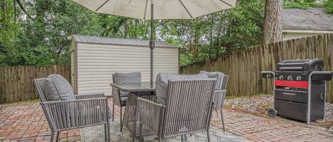 A patio with a table and chairs, a grill, and a shed.