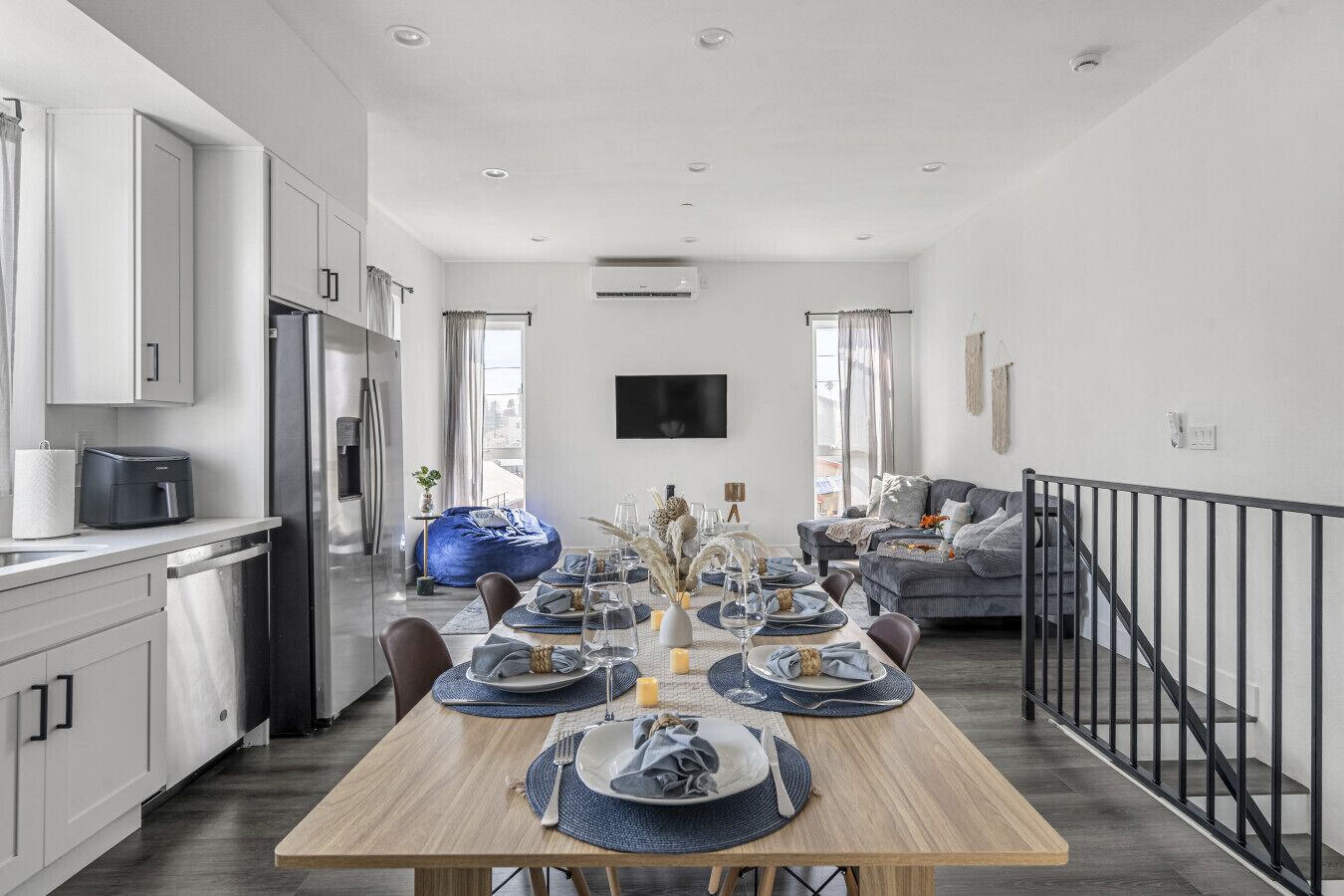 A modern kitchen and dining area with a wooden table set for a meal, a blue bean bag chair, and a grey sofa in the background.