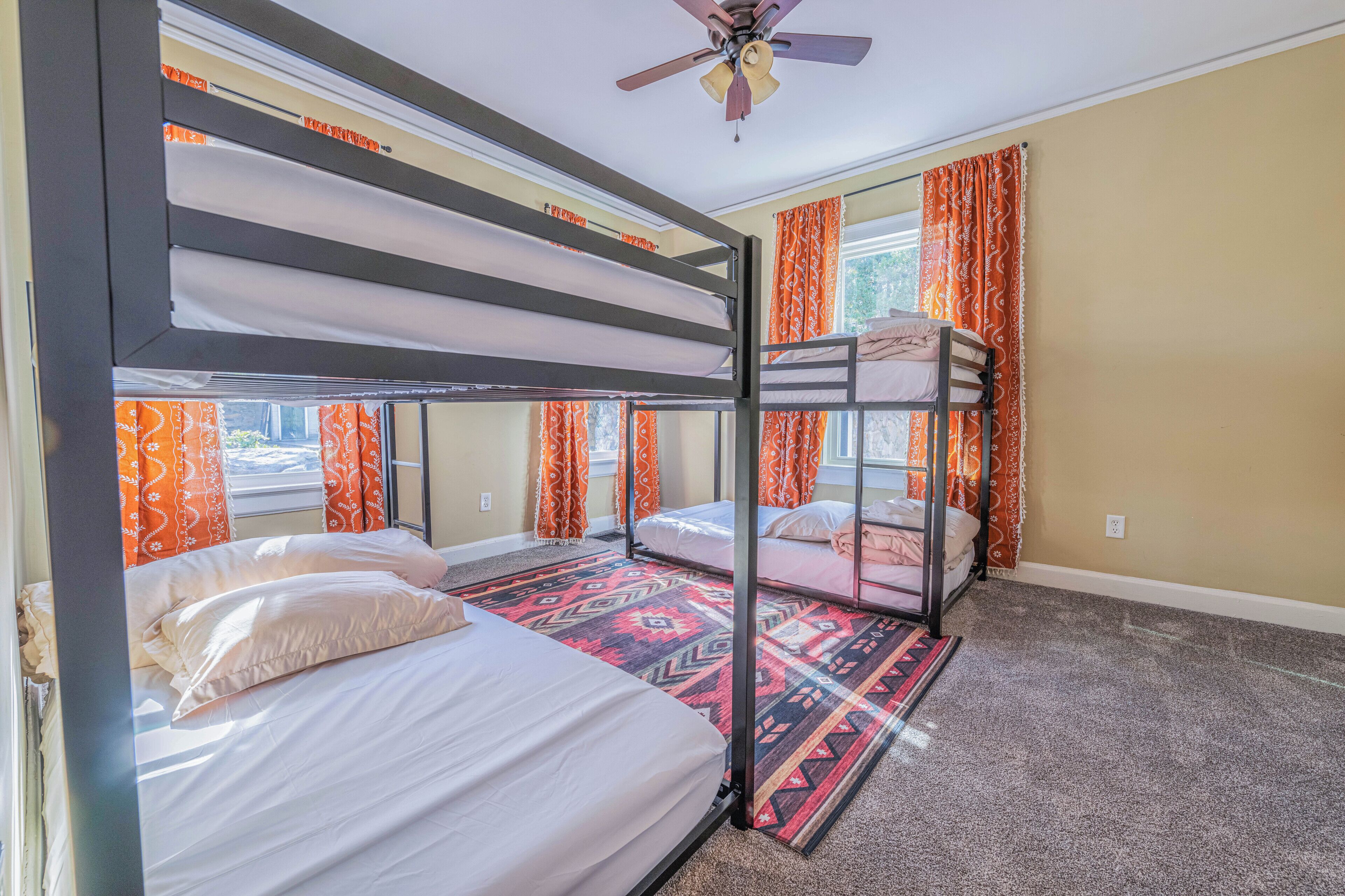 A room with bunk beds, a ceiling fan, and patterned curtains.