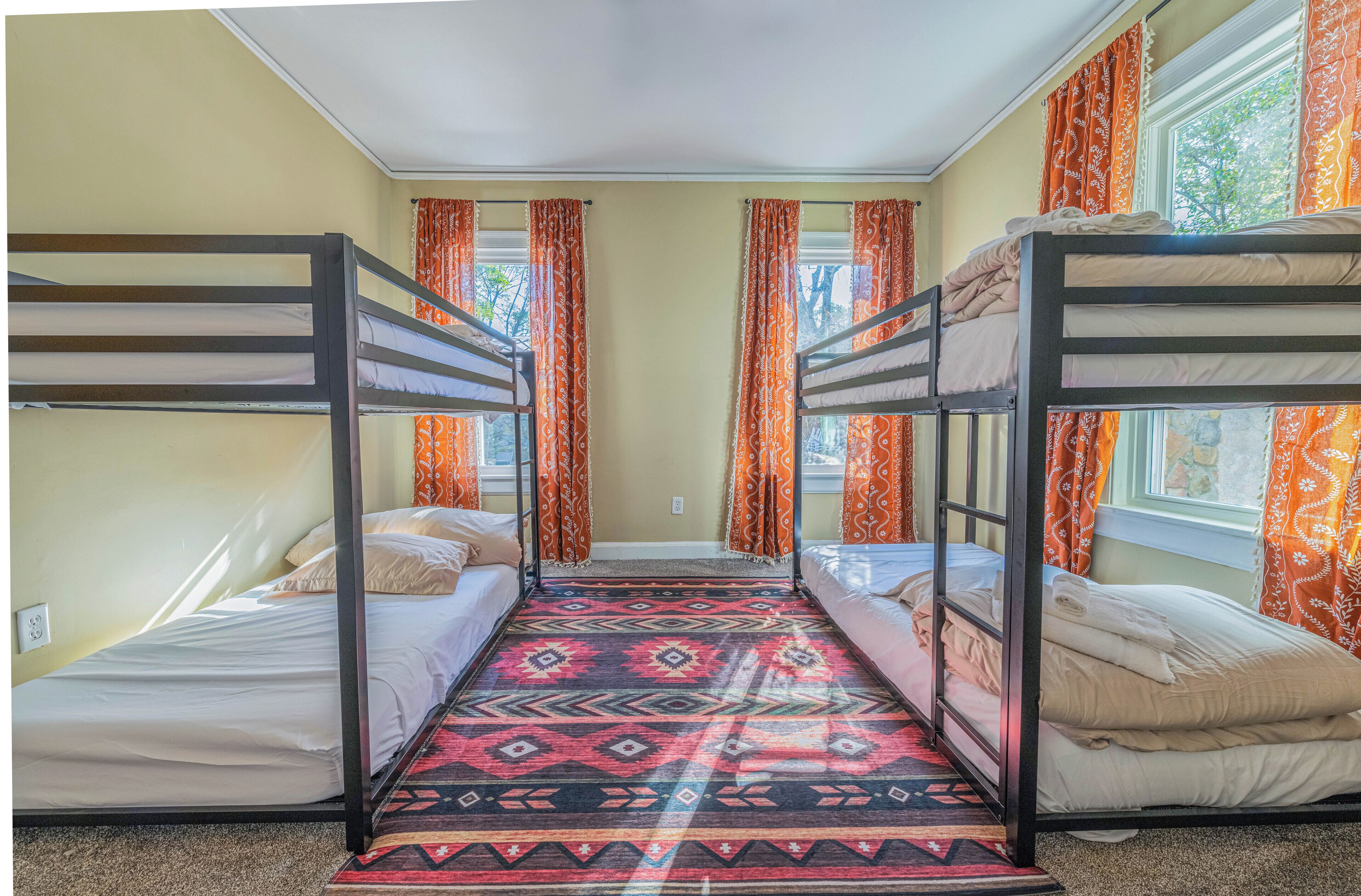 Une chambre avec des lits superposés, une moquette à motifs et des rideaux orange.