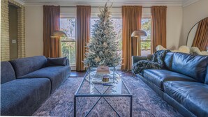 Un salon décoré d’un sapin de Noël, avec deux canapés, une table basse et de grandes fenêtres ornées de rideaux.