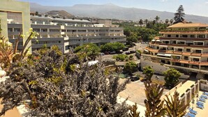 Un hotel con varios pisos, una zona de estacionamiento y vistas a montañas al fondo.