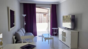 Una habitación con una cama, una mesita, un televisor y una puerta corredera que da a un espacio al aire libre.