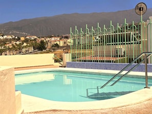 Una piscina amb vista a muntanyes, una tanca verda i un panell solar.