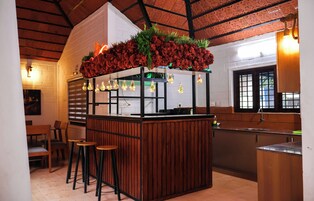 Un restaurante con una zona de bar de madera, taburetes y un arreglo floral decorativo en la barra.