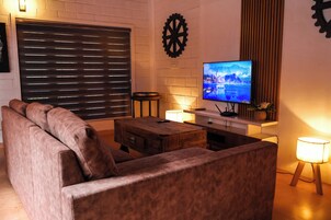 Una sala de estar con un sofá, una mesa de centro de madera, un televisor sobre un mueble bajo y una lámpara.