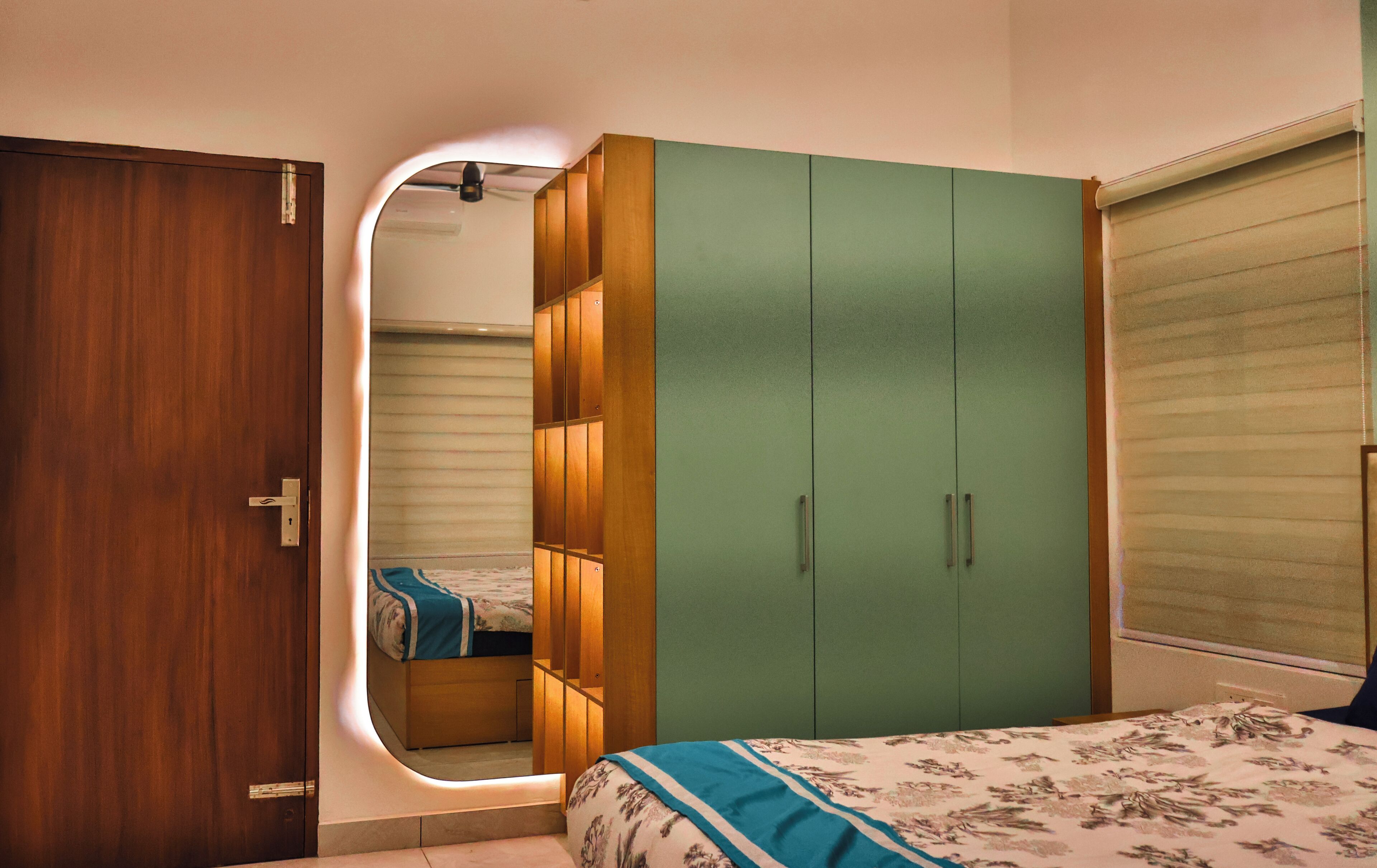 A bedroom with a wooden door, a green wardrobe, and a bed with a floral bedspread.