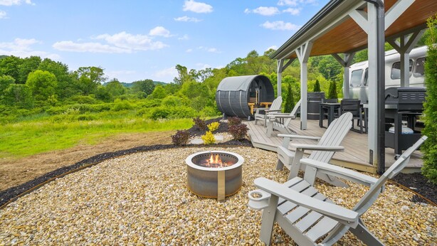 A covered outdoor seating area with Adirondack chairs, a fire pit, and a covered sleeping area with a large cylindrical object.
