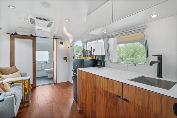A compact kitchen with a window, wooden cabinets, and a small refrigerator.