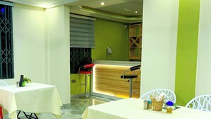A restaurant interior with marble flooring, white tables, red chairs, and a green accent wall. - Executive Key Hotel (Biseasi)