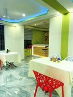 A restaurant interior with marble flooring, white tables, red chairs, and a green accent wall.