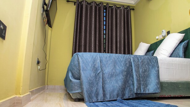 A hotel room with a bed, a flat-screen TV mounted on the wall, and a ceiling fan. - Executive Key Hotel (Biseasi)
