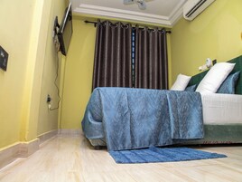 A hotel room with a bed, a flat-screen TV mounted on the wall, and a ceiling fan.