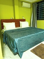 Quarto com cama, cabeceira de madeira, ar condicionado branco e janela com cortinas.