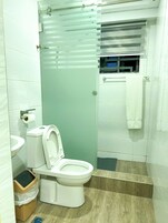 A small bathroom with a toilet, a trash bin, a towel hanging on the wall, and a shower area.