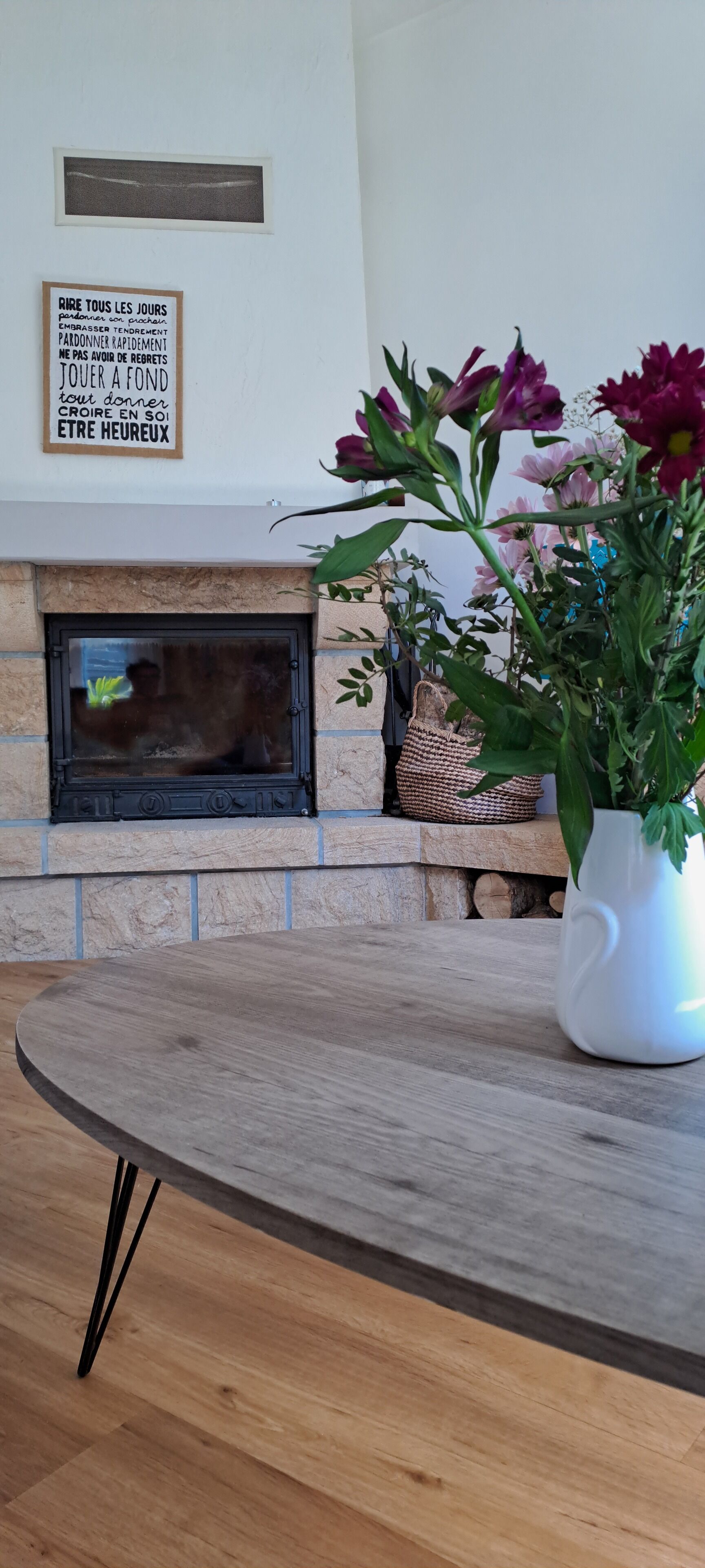 Ein Kamin mit Steinverkleidung, ein gerahmtes Zitat an der Wand und ein Tisch mit Blumen in einer Vase.