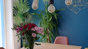 A dining area with a wooden table, yellow chairs, a vase with flowers, hanging rope lights, and a blue wall with a geometric decoration.