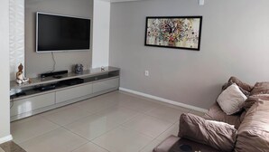 Un salon moderne avec un téléviseur à écran plat fixé au mur, une console sur laquelle sont posés des appareils électroniques, un canapé et un tableau abstrait encadré.