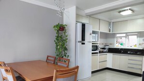 Une cuisine moderne avec des meubles blancs, un réfrigérateur blanc, un four à micro-ondes et une cuisinière. On y trouve une table à manger avec des chaises en bois et une plante suspendue.