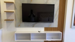 A modern living room with a large flat-screen TV mounted on a marble wall, wooden shelves, and a tufted sofa. - Escape to Cabo Tortuga. Apartment near the sea (Santa Marta)