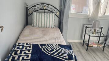 Un letto singolo con struttura in metallo, un cuscino a righe, una coperta con motivo blu e bianco e un comodino con dei libri.
