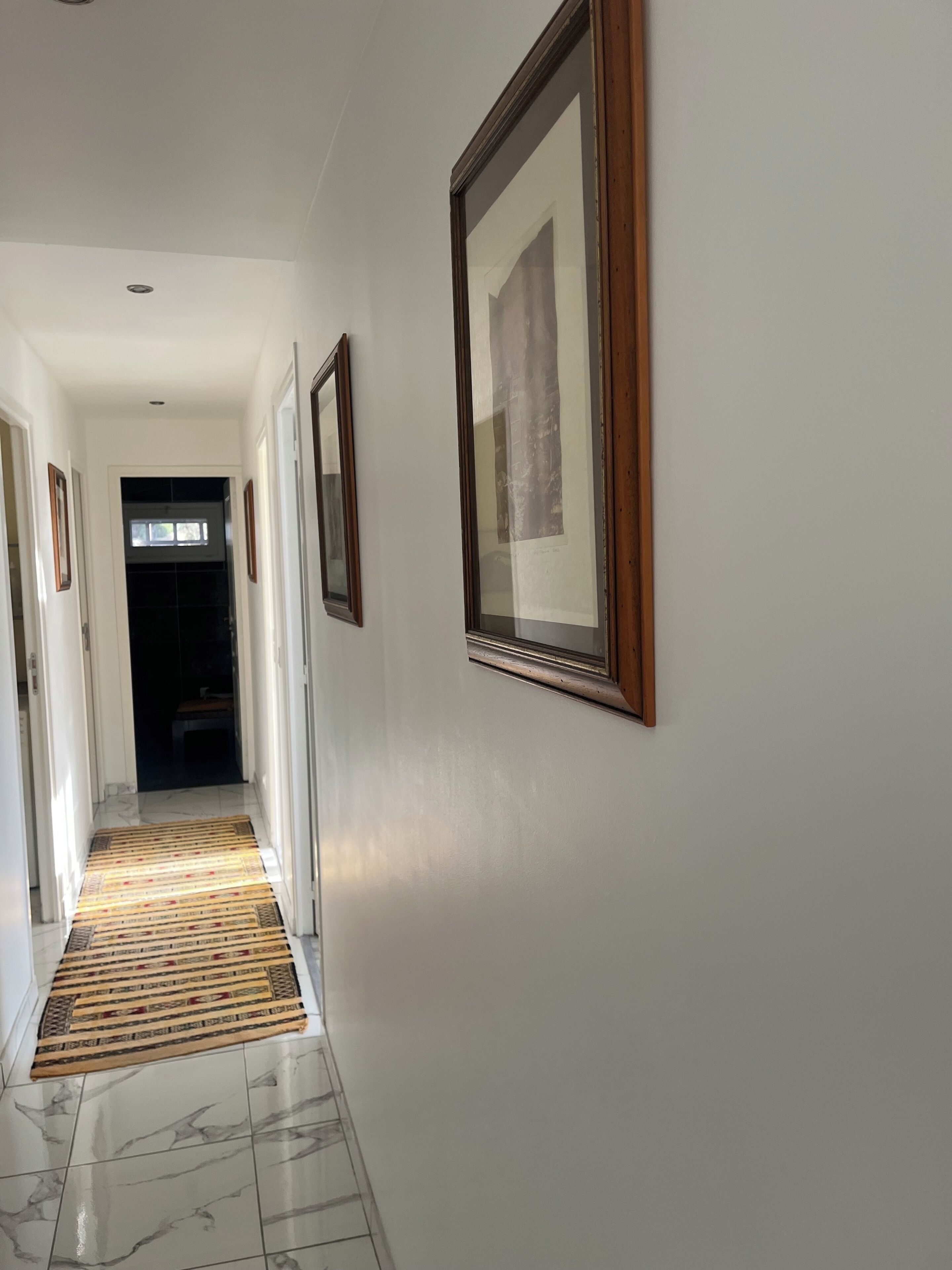 A hallway with framed pictures on the walls, a patterned rug on the floor, and a door at the end.