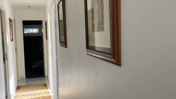 A hallway with framed pictures on the walls, a patterned rug on the floor, and a door at the end.