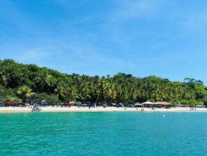 Una platja amb aigua turquesa cristal·lina, palmeres i sombrerelles de platja.