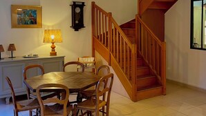 Ein Essbereich mit Holztisch und Stühlen, einer Wanduhr und einer Treppe, die in eine obere Ebene führt.