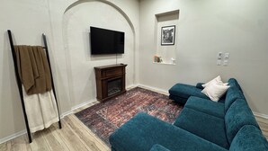 Ein Wohnzimmer mit Fernseher, Kamin, Sofa und einem gemusterten Teppich.