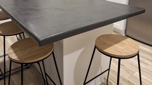 Eine moderne Küche mit einer zentralen Kochinsel, schwarzen Barhocker, einer Edelstahl-Dunstabzugshaube und einem Geschirrspüler.