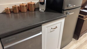 Eine Küche mit Geschirrspüler, Kaffeemaschine und mehreren Kupferbehältern auf der Arbeitsfläche.