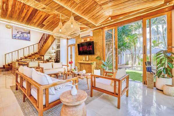 A spacious living area with a wooden ceiling, a staircase, a fireplace, and a large TV screen displaying 'NETFLIX'. - Villa Chicago, Spacious 7 BDR, lively area (Kabupaten Badung)