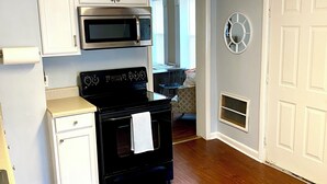 A compact kitchen with white cabinets, a black stove, a microwave, and a small countertop.