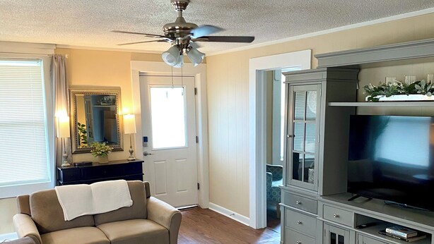 A living room with a sectional sofa, a round ottoman, a television on a cabinet, and a ceiling fan.