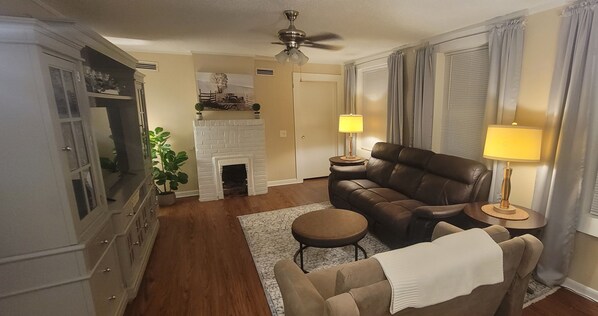 A living room with a fireplace, leather sofa, and a dining area with a lamp.
