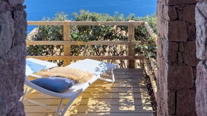A wooden deck with a view of the sea, a lounge chair, and a stone wall.