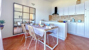 A compact kitchen with white cabinets, a tiled backsplash, and a dining area with wicker chairs and a table.