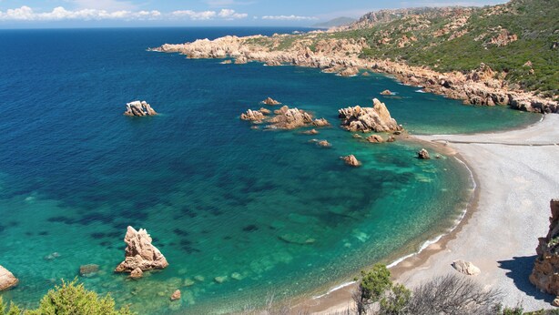 A coastal landscape with clear turquoise waters, rocky outcrops, and a sandy beach.