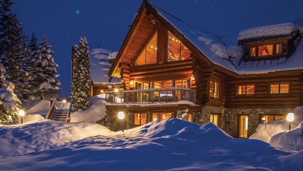 Una cabaña de troncos con balcón, rodeada de nieve, de noche.