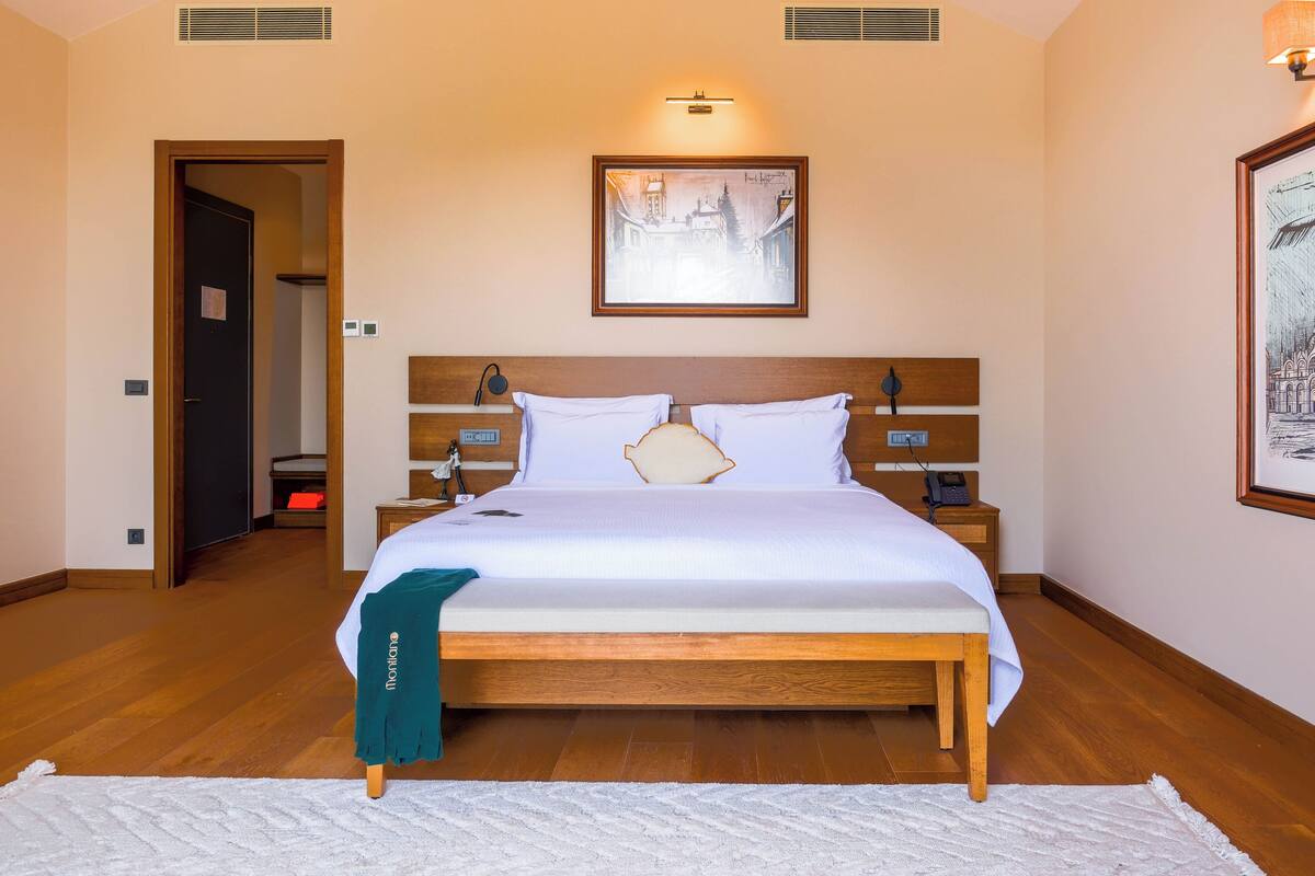Ein Hotelzimmer mit einem großen Bett, einem Holz-Kopfteil, Nachttischen, einer Nachttischlampe und einem gerahmten Bild über dem Bett.