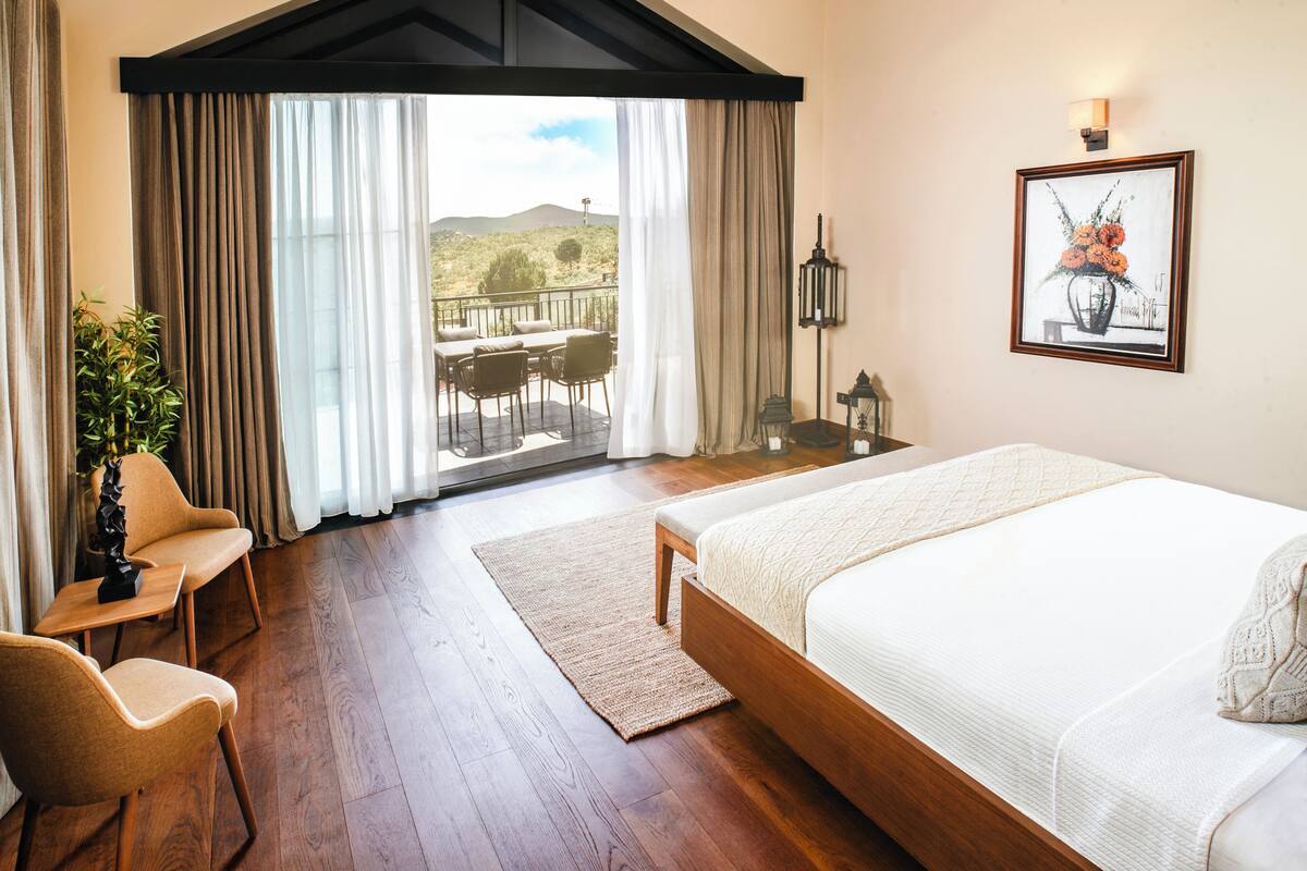 Ein Schlafzimmer mit einem großen Bett, Blick auf einen Balkon mit Sitzmöbeln und einem Bild an der Wand.