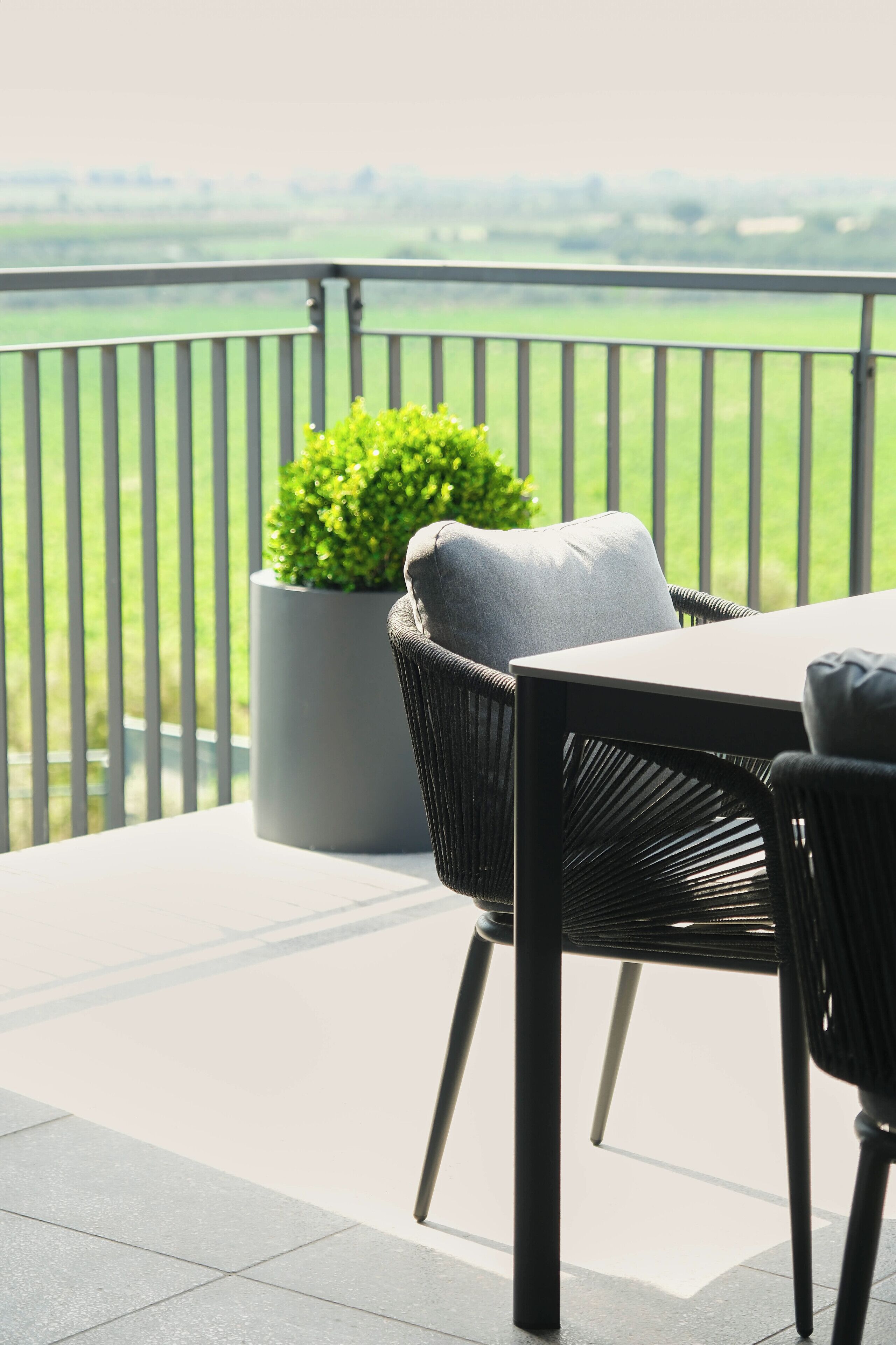 A balcony with a table and chairs, a potted plant, and a view of a green landscape.