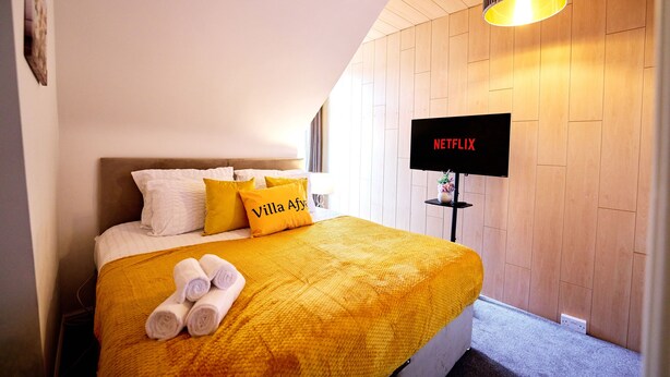 Una habitación de hotel con una cama, un televisor montado en la pared y una lámpara en el techo.