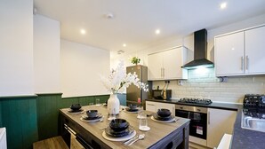 Una cocina moderna con armarios blancos, una mesa de comedor de madera dispuesta con platos y tazones, un florero con flores y una estufa.