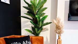 Una sala de estar moderna con un sofá, una planta en maceta, un florero con flores secas y una mesita de madera con un control remoto.