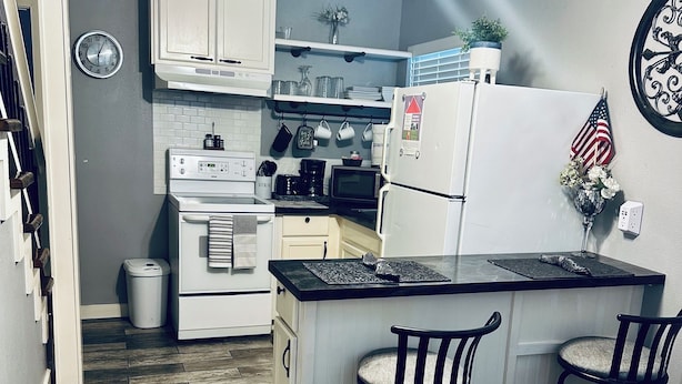 Una cucina compatta con isola centrale, mobili bianchi e ventilatore a soffitto.